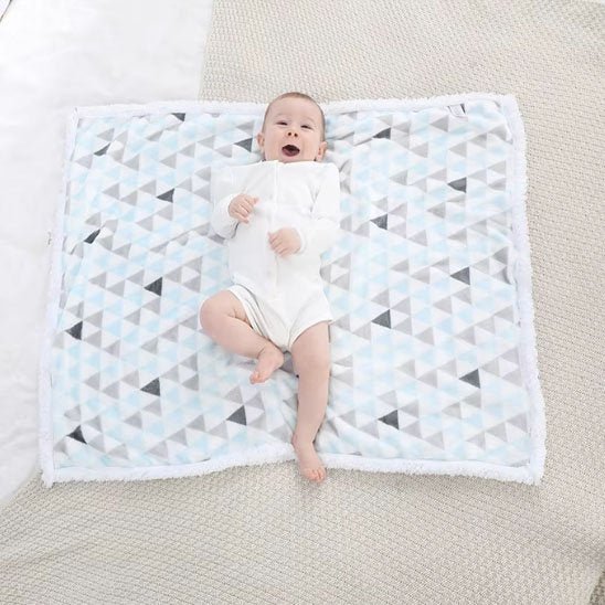 Bébé allongé sur couverture bébé moelleuse design triangles apaisants.