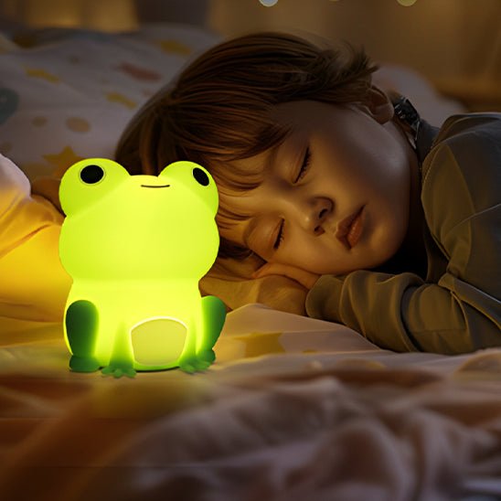 Enfant dormant paisiblement près d’une veilleuse grenouille diffusant une lumière douce.