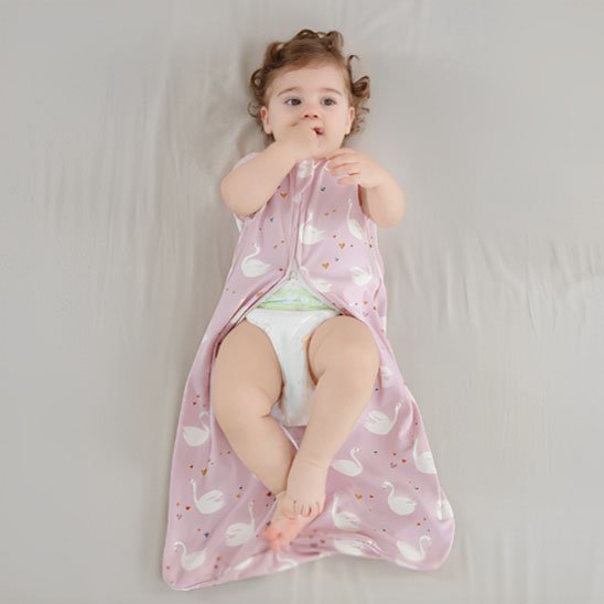 Bébé allongé sur un lit, vêtu d’une gigoteuse rose à motifs de cygnes blancs.