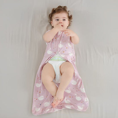 Bébé allongé sur un lit, vêtu d’une gigoteuse rose à motifs de cygnes blancs.