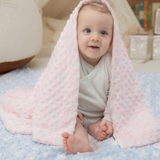 Bébé assis sous couverture bebe rose douce dans ambiance chaleureuse