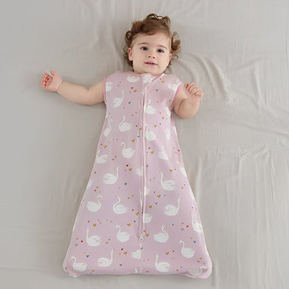 Bébé calme allongé sur un lit, vêtu d’une gigoteuse rose à motifs de cygnes blancs