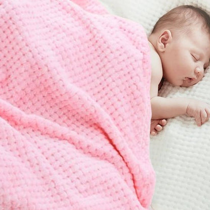 Bébé dormant paisiblement sous une couverture bébé rose en coton gaufré doux.