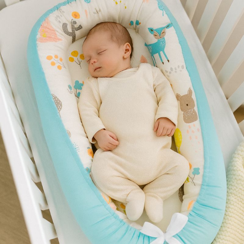 Bébé endormi dans réducteur turquoise à motifs forêt pastel : lapin, faon et feuillage