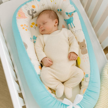 Bébé endormi dans réducteur turquoise à motifs forêt pastel : lapin, faon et feuillage