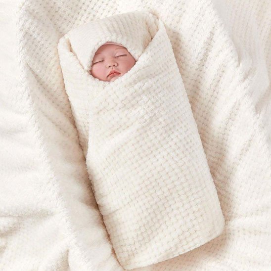 Bébé emmailloté dans une couverture bébé crème douce en coton gaufré texturé.