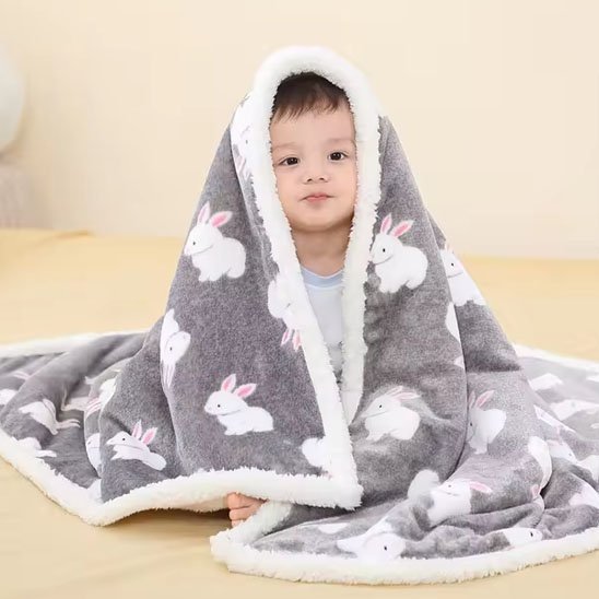 Bébé enveloppé dans couverture grise avec motifs lapins blancs et roses, ambiance douce.