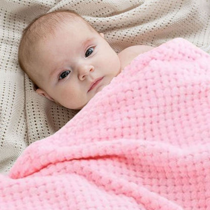 Bébé regardant la caméra sous une couverture bébé rose douce en coton gaufré.