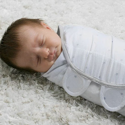 Couverture d’emmaillotage blanc étoiles bébé dormant paisiblement sur tapis doux.