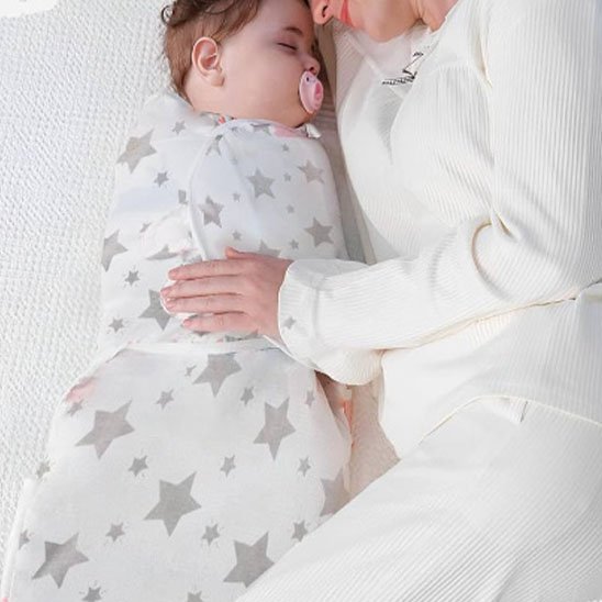 Couverture d’emmaillotage blanc étoiles bébé dormant paisiblement auprès de maman.