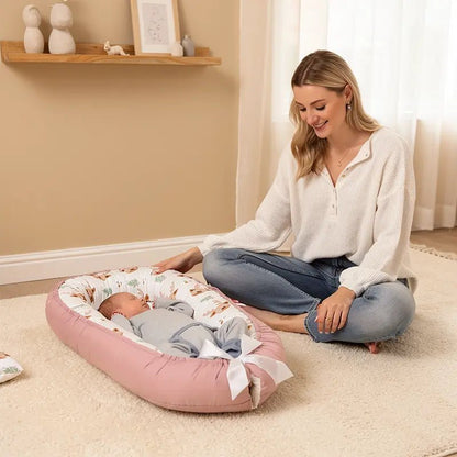 Bébé allongé dans un réducteur de lit rose poudré avec motif cerf, pendant que sa maman assise à côté le regarde avec douceur.