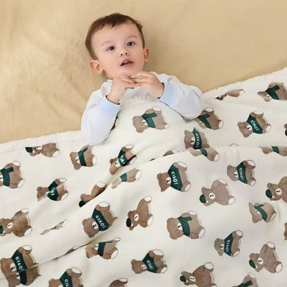 Enfant allongé sous couverture bébé blanche avec oursons bruns en chemise verte "LOVED".