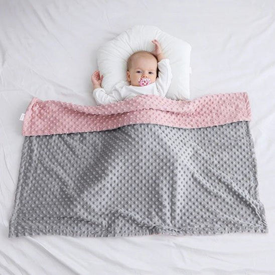 Enfant endormi sous couverture bébé rose et grise à texture douce.