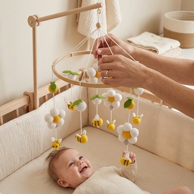 Maman fixe le mobile pendant que bébé observe joyeusement. 
