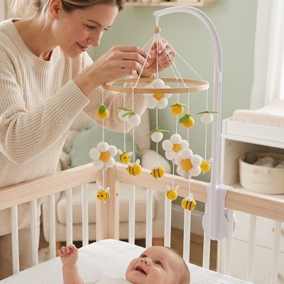 Maman installe doucement le mobile pendant que bébé regarde émerveillé.