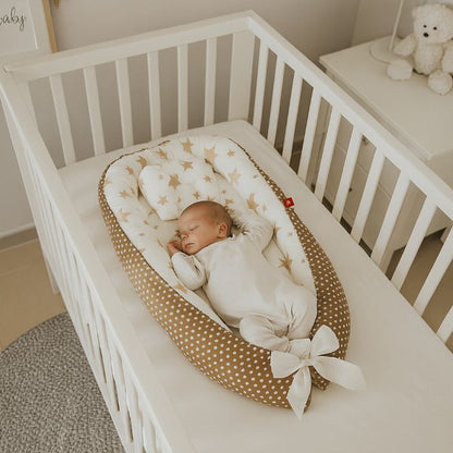 Bébé endormi paisiblement dans un nid douillet décoré d’étoiles dorées, posé dans un lit blanc sécurisé.