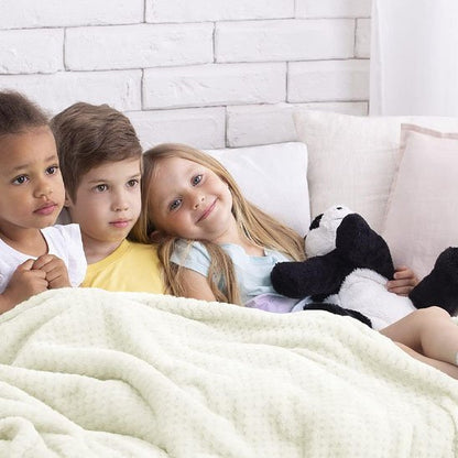 Trois enfants assis sur un lit sous une couverture bébé blac.